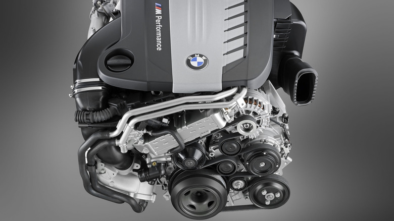 A silver BMW N57 Inline-Six engine model against a slate gray background, top and front view shown.