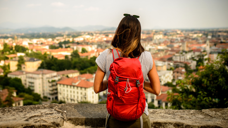 woman with red backpack overlooking small city 