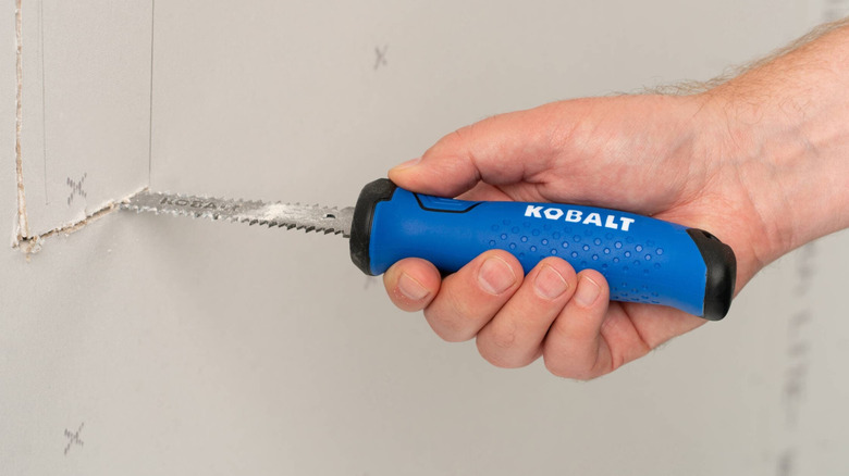 A hand using a Kobalt jab saw to cut drywall