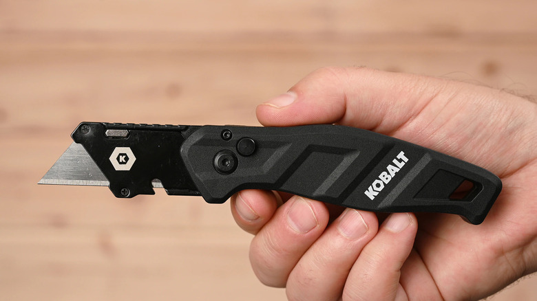 A hand holding a black Kobalt utility knife