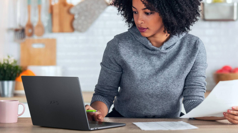 A person using a black Dell XPS 14 on a kitchen counter.