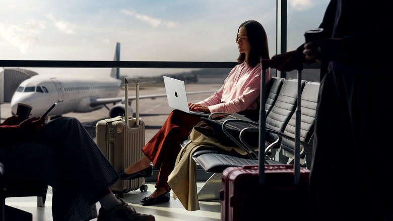 A woman working on a MacBook Pro in an airport departure lounge.