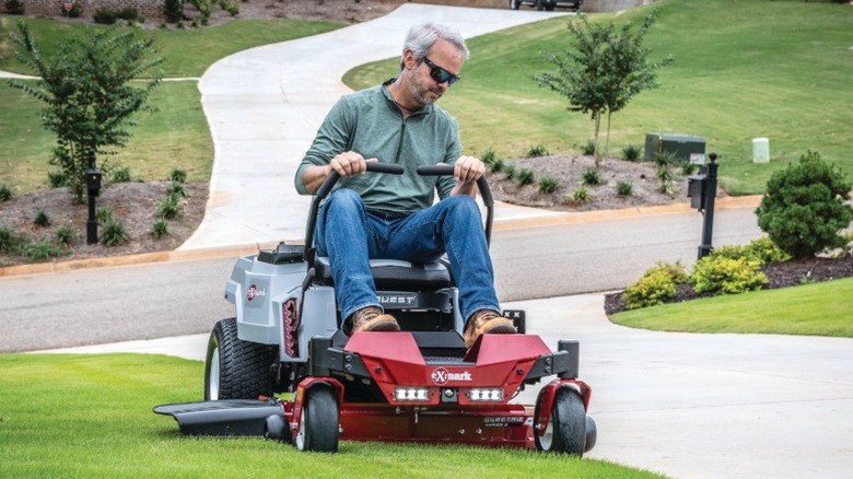 Person on an Exmark zero-turn mower next to a concrete driveway