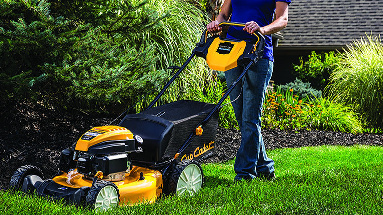 A person pushes a yellow Cub Cadet mower on a lawn.