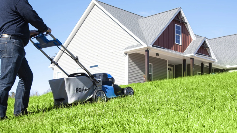 A person using a Kobalt 80V mower to cut a sloping yard