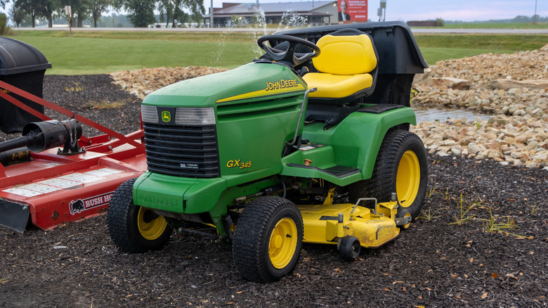 A John Deere mower parked on some soil, front 3/4 view