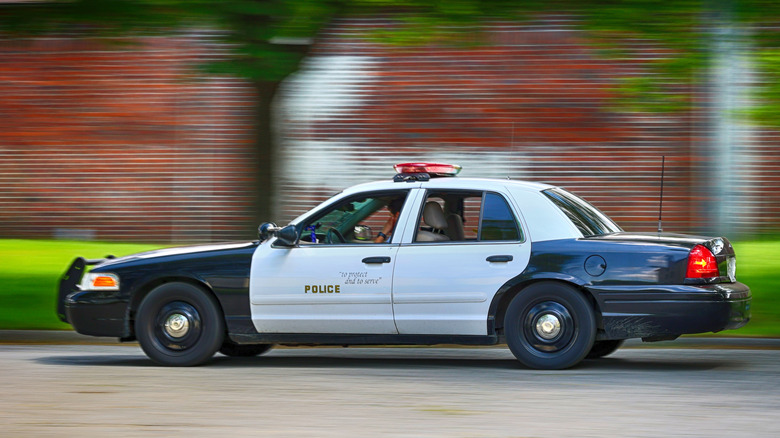Side view of black and white Ford Crown Victoria Police Interceptor driving on city street.