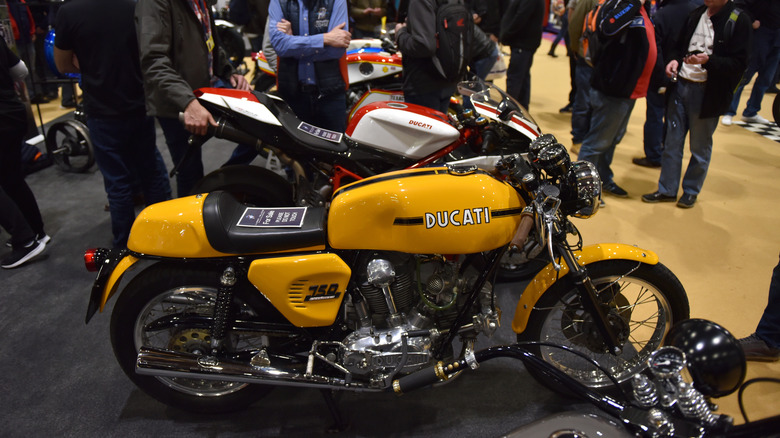 A yellow and black 1960s Ducati 750 Sport on display to a crowd during the MCN London motor show.