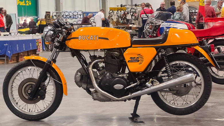A yellow Ducati 750 cafe racer motorcycle, finished here in the "Sport" trim with black racing stripe parked indoors.