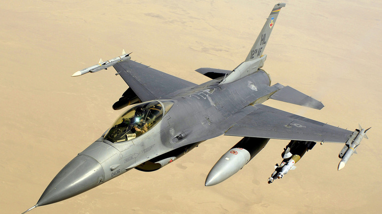 An F-16 Fighting Falcon flying with desert ground underneath