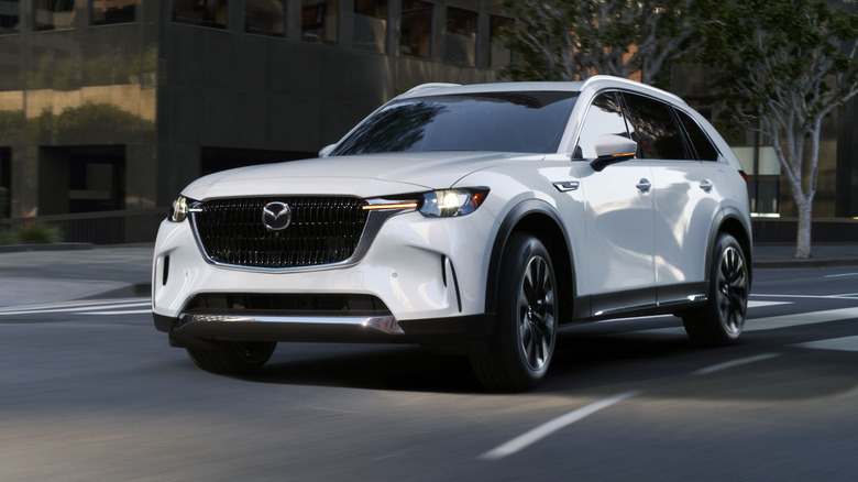 Mazda CX-90 PHEV cornering at speed in the city, front 3/4 view, white exterior