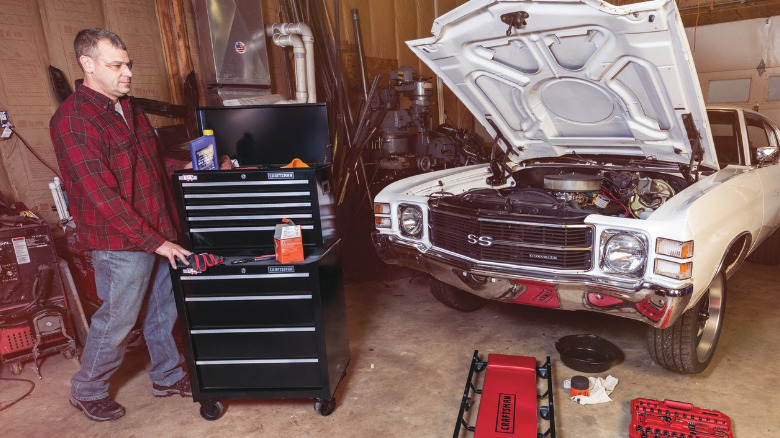 A person moves a Craftsman rolling tool cabinet next to a car in a garage.