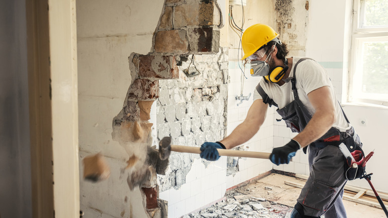 construction worker demolishing wall with sledgehammer 