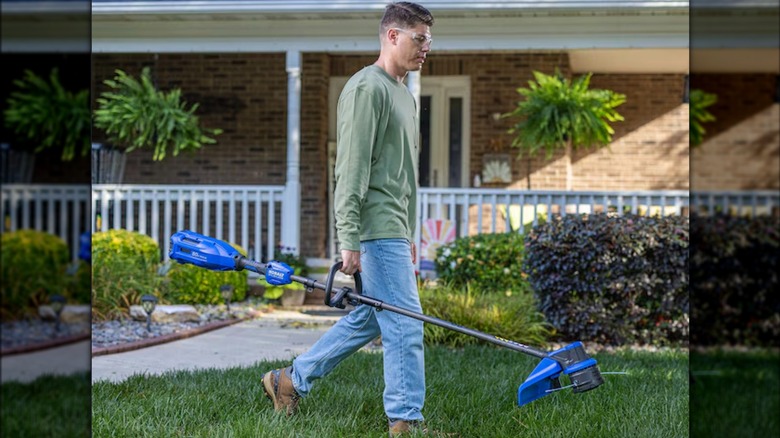 Person carrying Kobalt 80V 17-inch Straight Shaft String Trimmer across yard