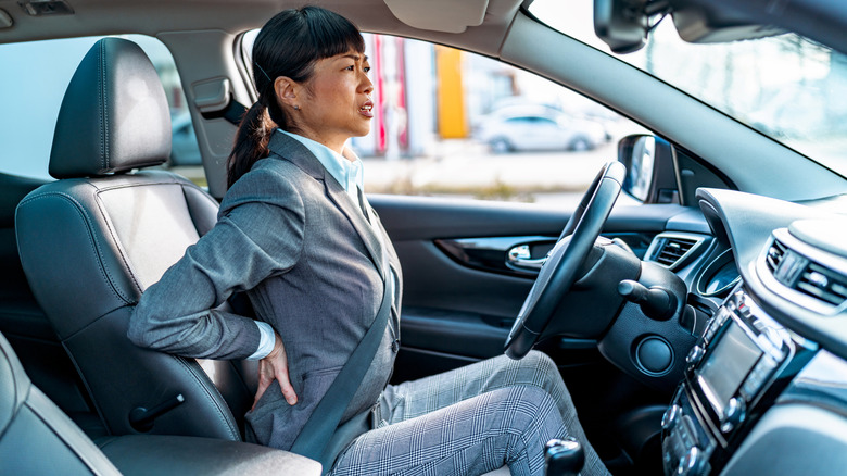A female driver behind the wheel of a car, enduring back pain.