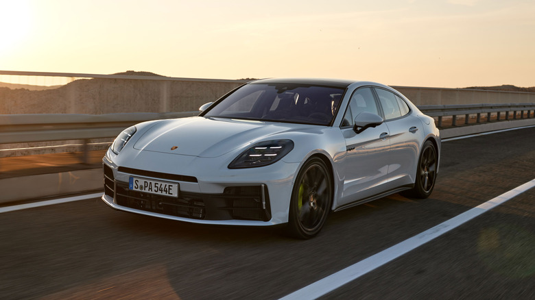 A white hybrid Porsche Panamera sedan being driven on a smooth road during sunset, front 3/4 view
