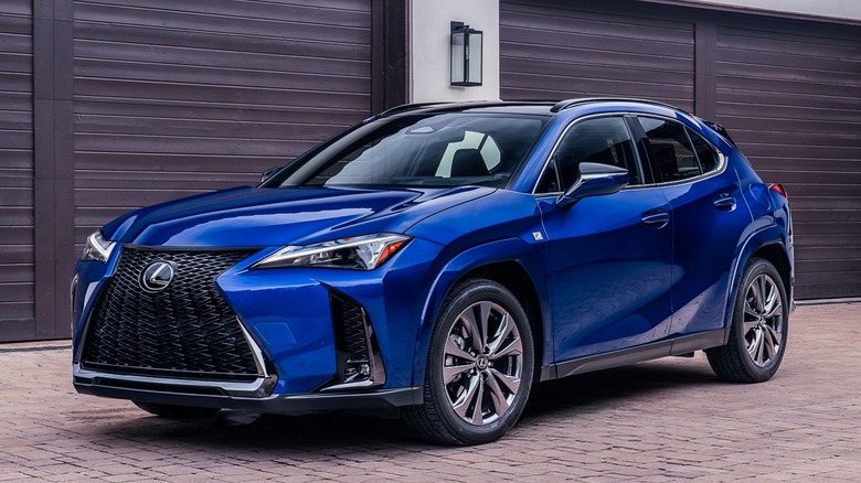 Front 3/4 view of 2026 Lexus UX300h on brick surface in front of garages