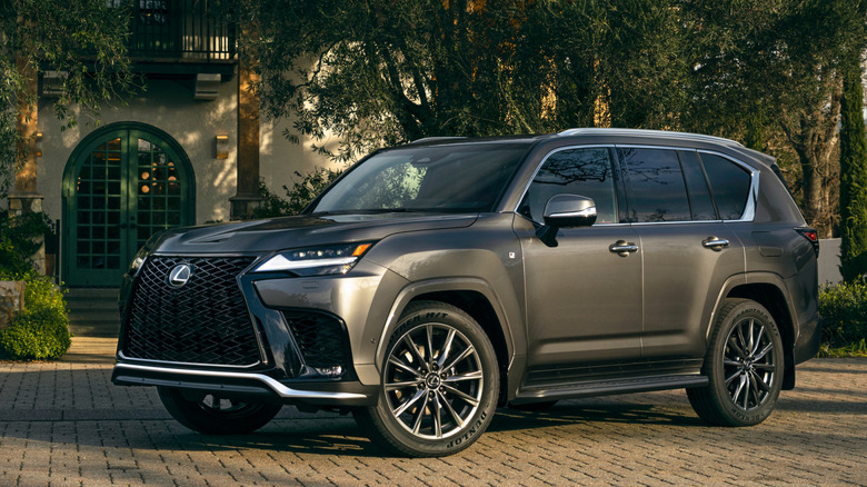 2026 Lexus LX700h hybrid in front of classical home with greenery, front-left 3/4 view