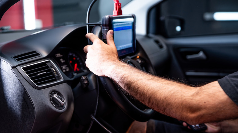 Auto mechanic holding a diagnostic tool resting on a car's steering wheel
