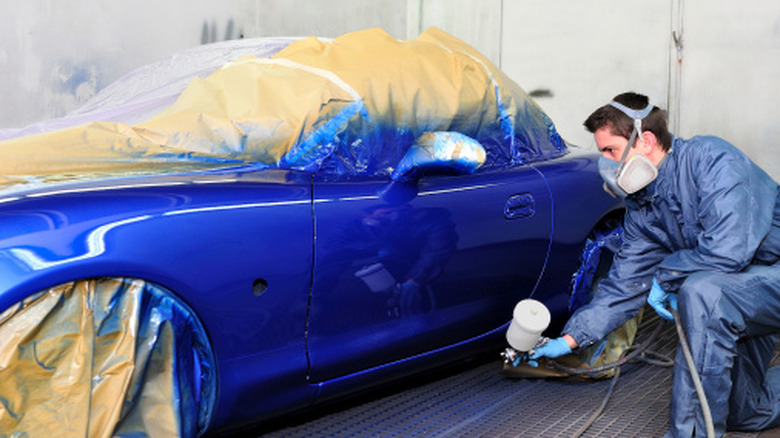 Auto technician spraying Mazda MX-5 with blue paint in professional paint booth