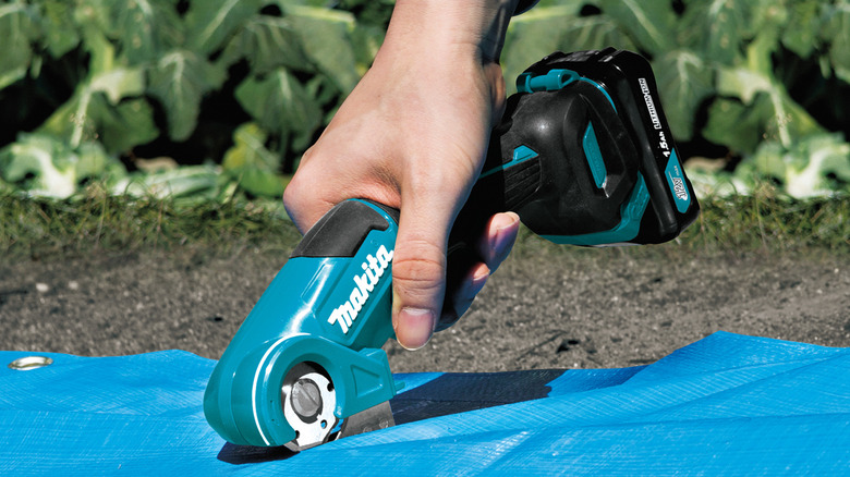 Makita 12V CXT multi-cutter tool being used outside to cut tarpaulin.