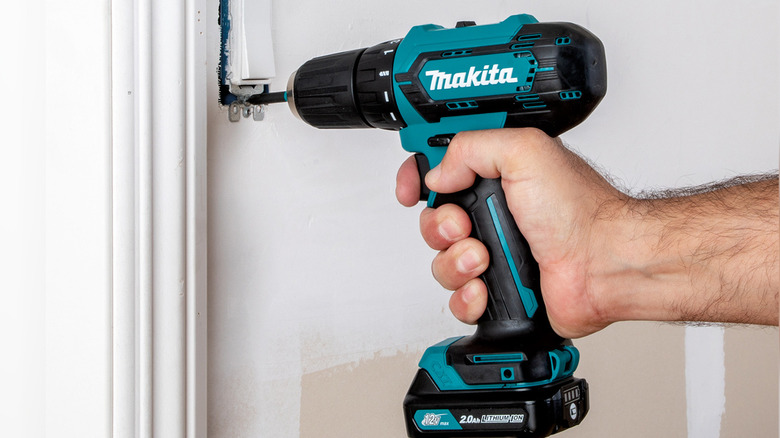 Makita 12V max CXT driver-drill being used to unscrew a light switch from a wall.