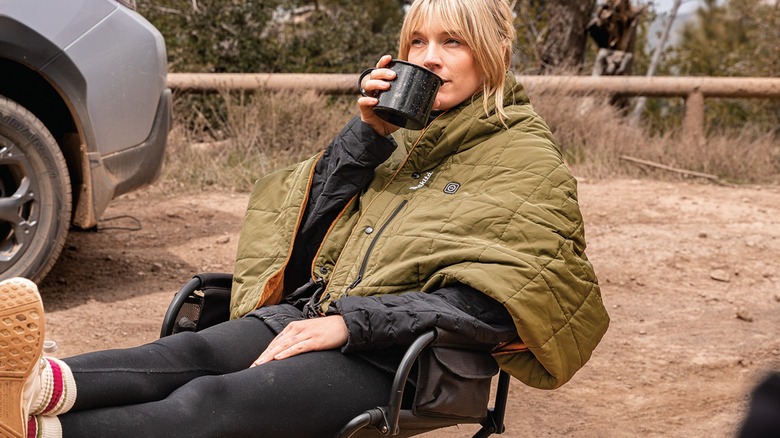 Camper sitting on a folding chair wearing an Outdoor Adventure heated blanket.
