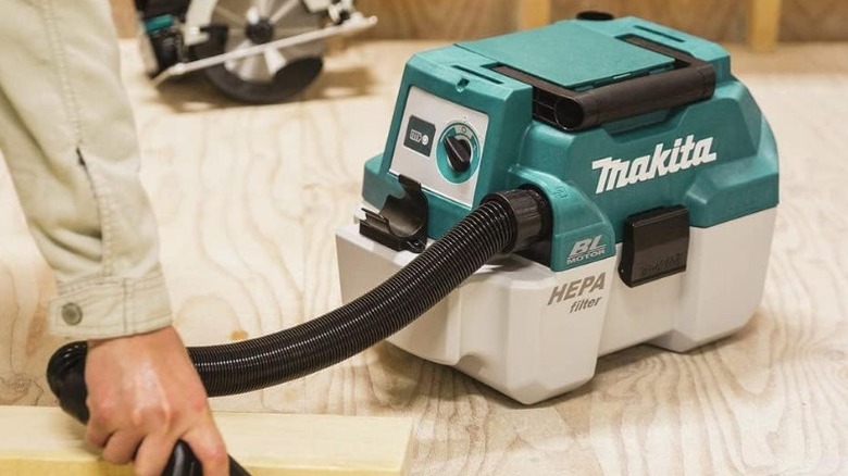 Person cleaning sawdust with Makita XCV11Z 18V LXT Brushless 2-Gallon HEPA Portable Wet/Dry Shop Vacuum