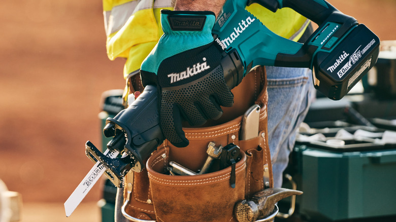 A worker carrying a Makita reciprocating saw while wearing Makita gloves.