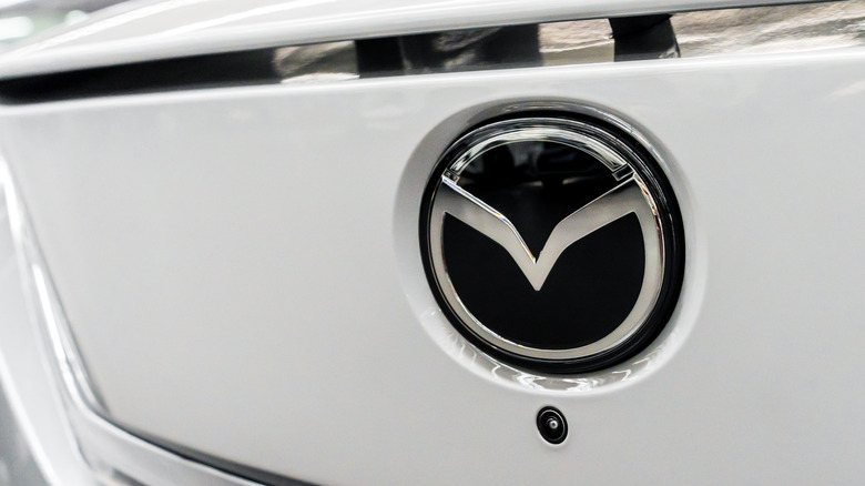 A close-up of a white car's rear-mounted Mazda badge.