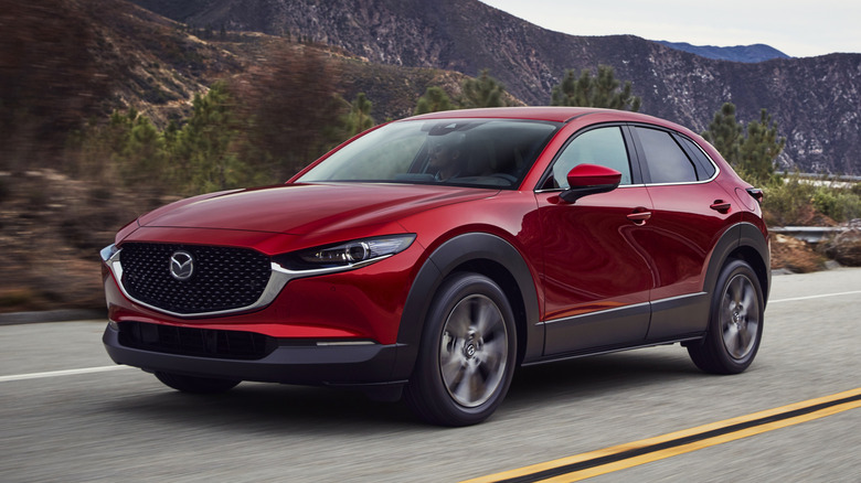 A red Mazda CX-30 SUV being driven through a rural setting road.