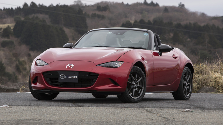 A red Mazda MX-5 Roadster parked in front of a hill.