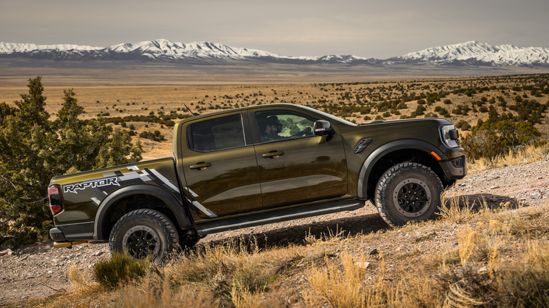 Side view of gold Ford Ranger Raptor climbing hill on desert off road trail.