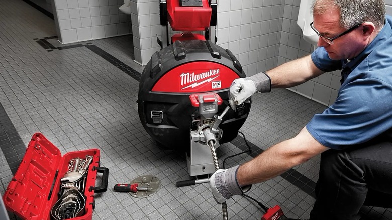A person using a Milwaukee sewer drum machine on a drain.