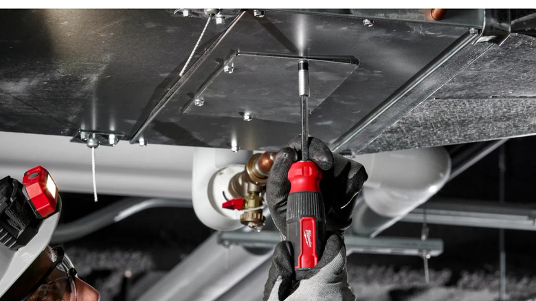 Man using Milwaukee multi-bit screwdriver on metal panel
