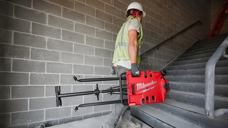 Man walking up steps with Milwaukee leveling tripod