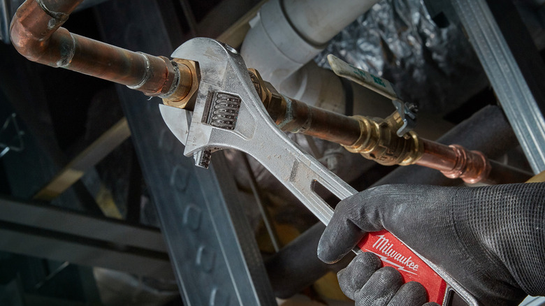 A Milwaukee 12-inch Adjustable Wrench used to tighten a metal tube.