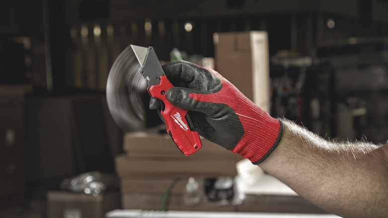 A Milwaukee Fastback 6-in-1 Folding Utility Knife held by a gloved hand.