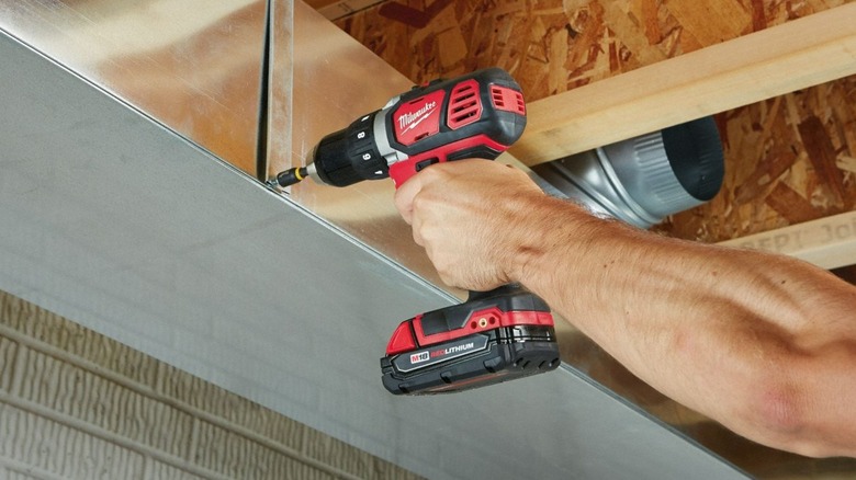 A person using a Milwaukee M18 drill on metal.