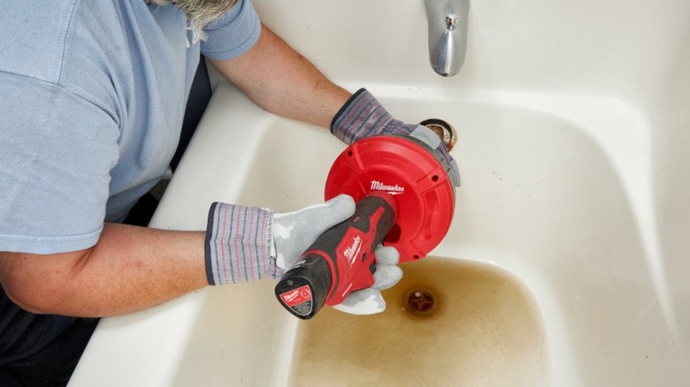 A person using a Milwaukee auger on a bathtub drain.