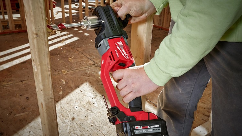 A worker drilling a right-angle hole in stud with a Milwaukee Hole Hawg