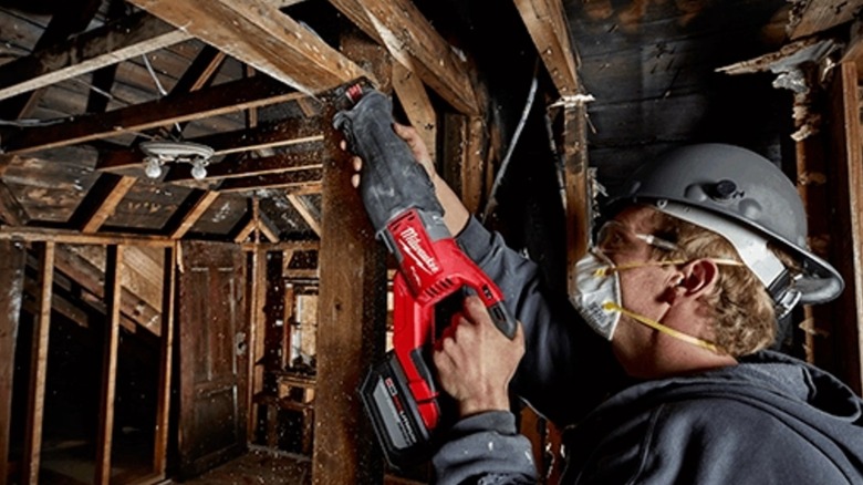 Worker in hard hat and face mask cutting timber beam with a Milwaukee Super Sawzall