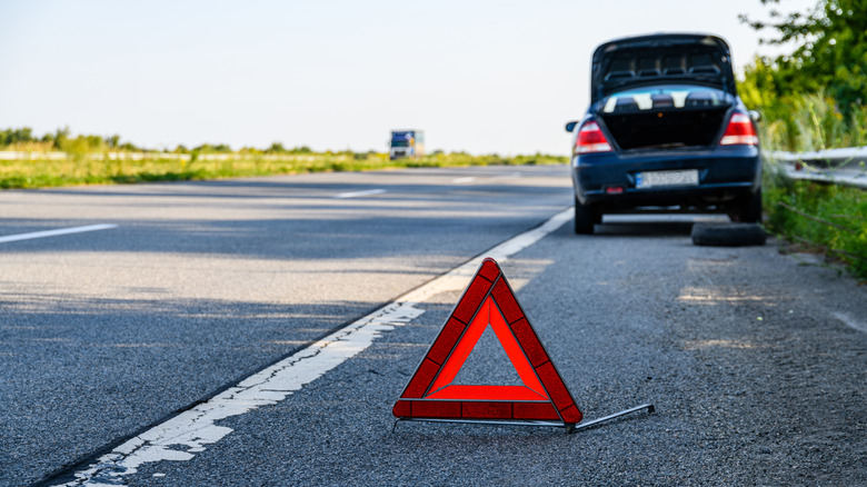 Car on the side of the road with its trunk raised and an orange triangle behind it