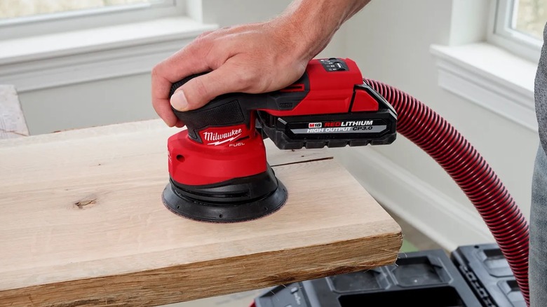 A person using a Milwaukee random orbit sander.
