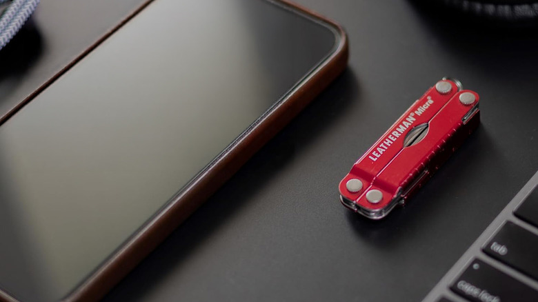 A red Leatherman Micro on a table next to a smartphone.