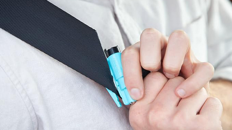 A person cutting their seatbelt with a Resqme emergency keychain tool.