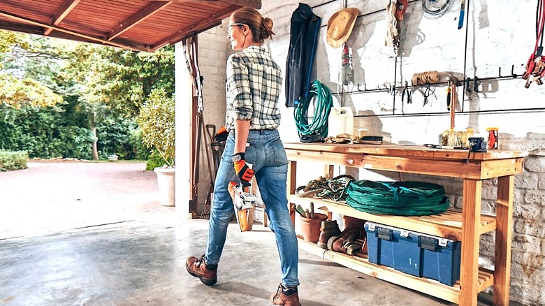 Person walking out of a garage carrying a Stihl mini chainsaw