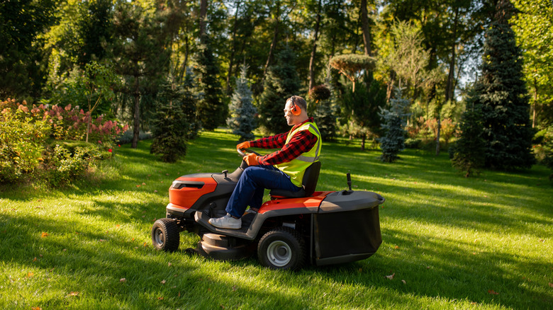 A gardener operating riding lawn mower on green grass