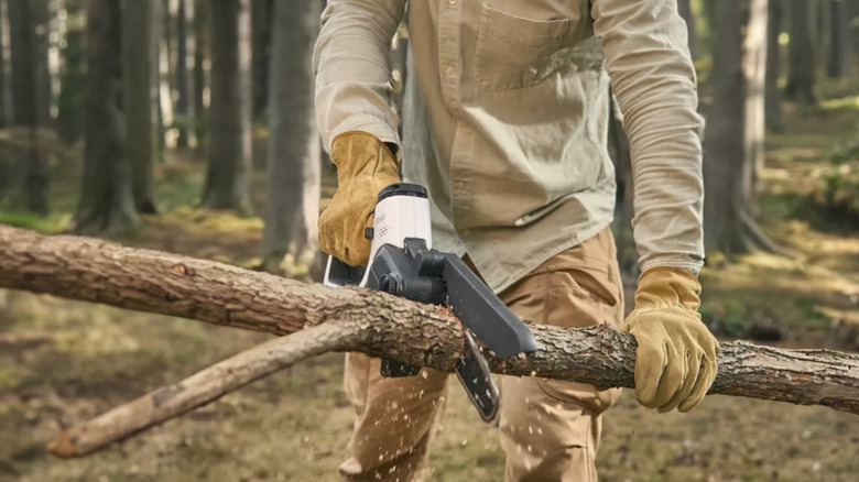 Two gloves hands using a mini Litheli chainsaw to cut a fallen tree