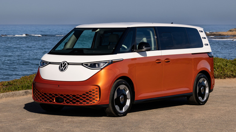Front 3/4 view of orange and white Volkswagen ID. Buzz parked at beach.